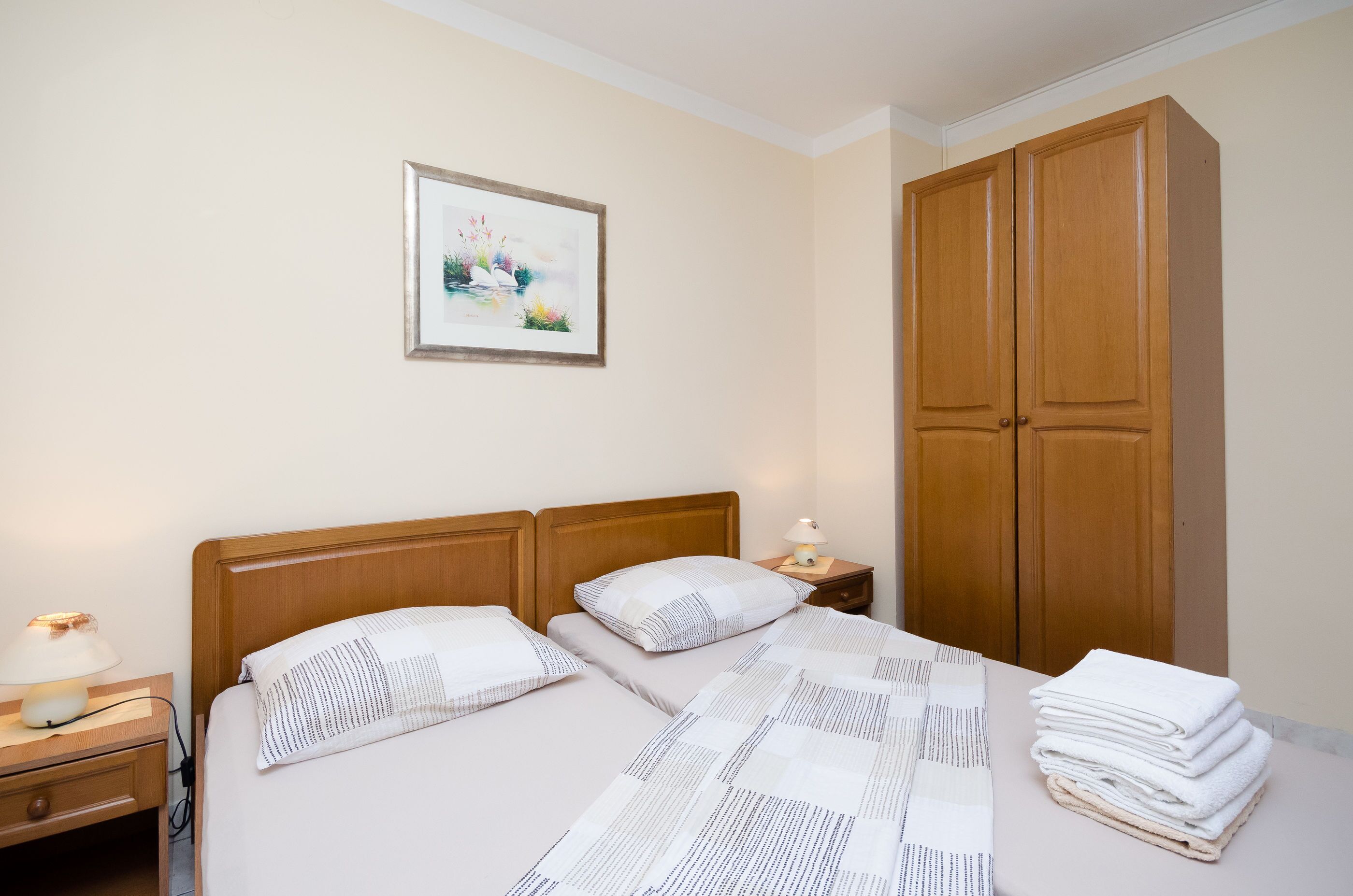 A neatly made bed with a patterned bedspread and pillows, a bedside lamp, a framed picture on the wall, and a wooden wardrobe.