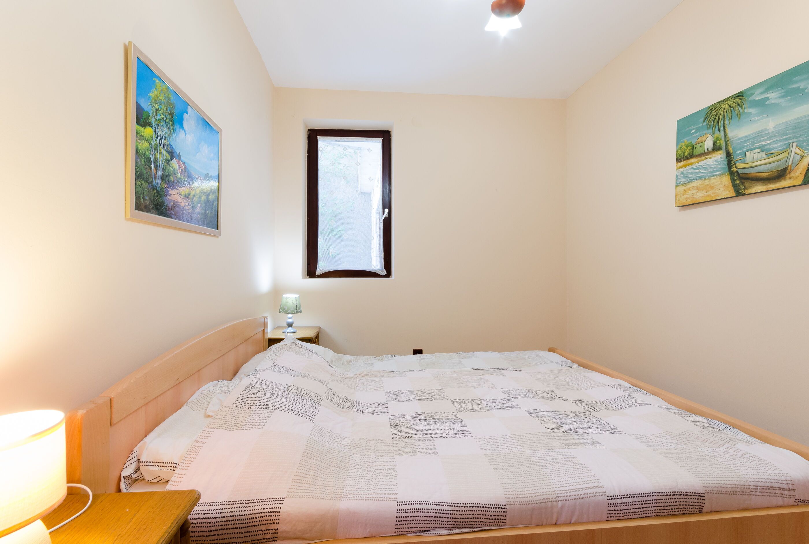 A bedroom with a bed, a nightstand, a lamp, and two paintings on the walls.