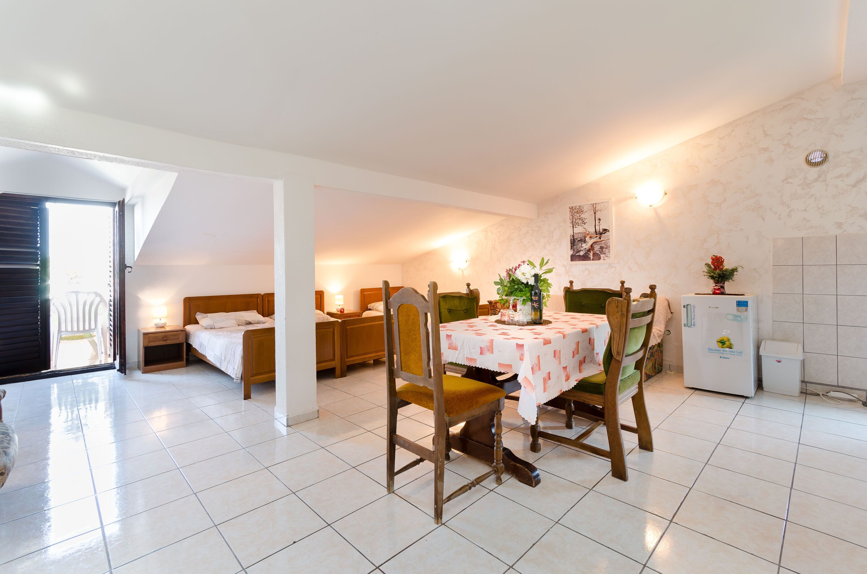 Een ruime kamer met een eettafel, stoelen, een bed en een koelkast.