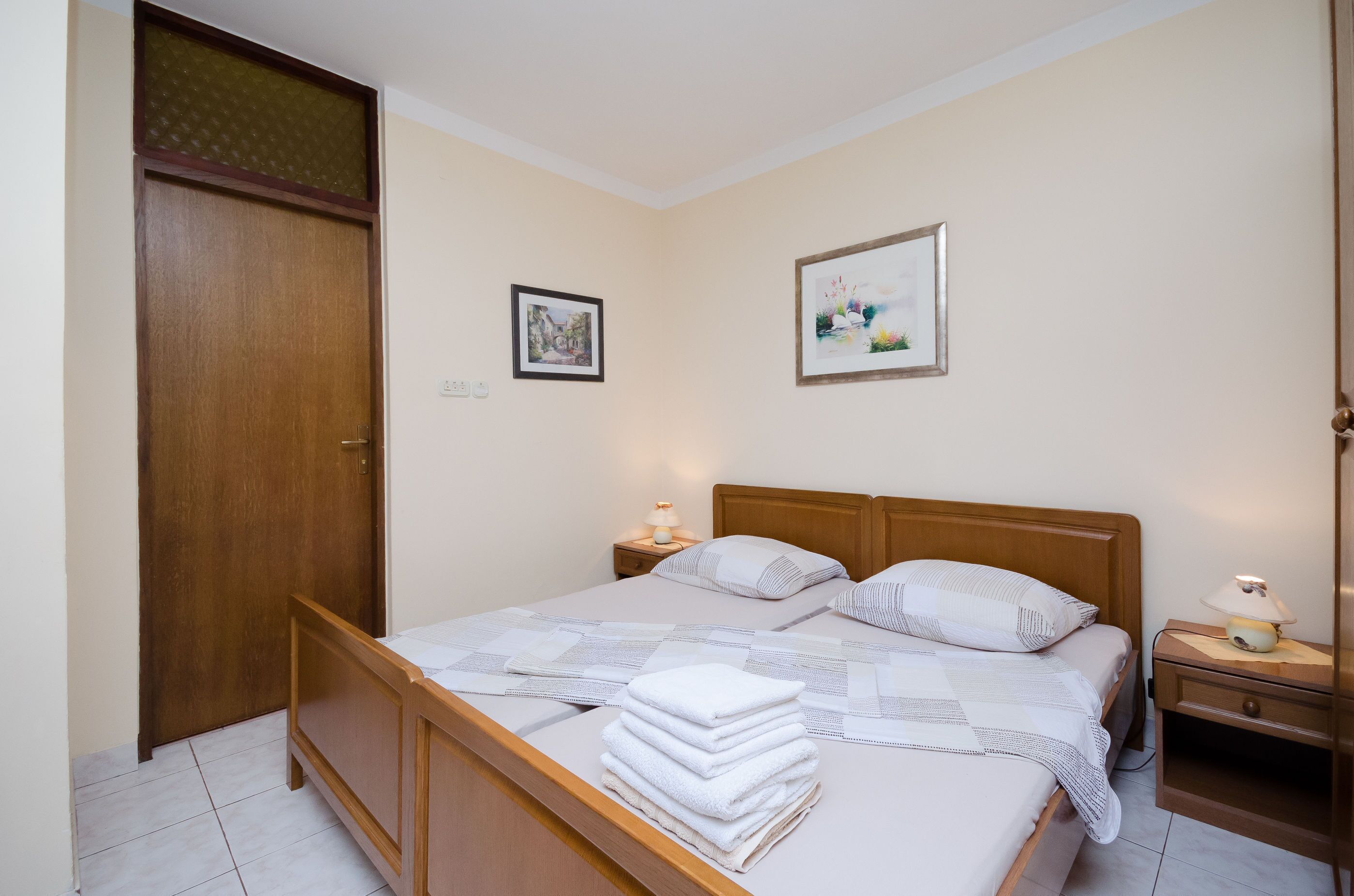 A neatly made double bed with a wooden headboard, two bedside tables with lamps, and a door with a decorative panel.