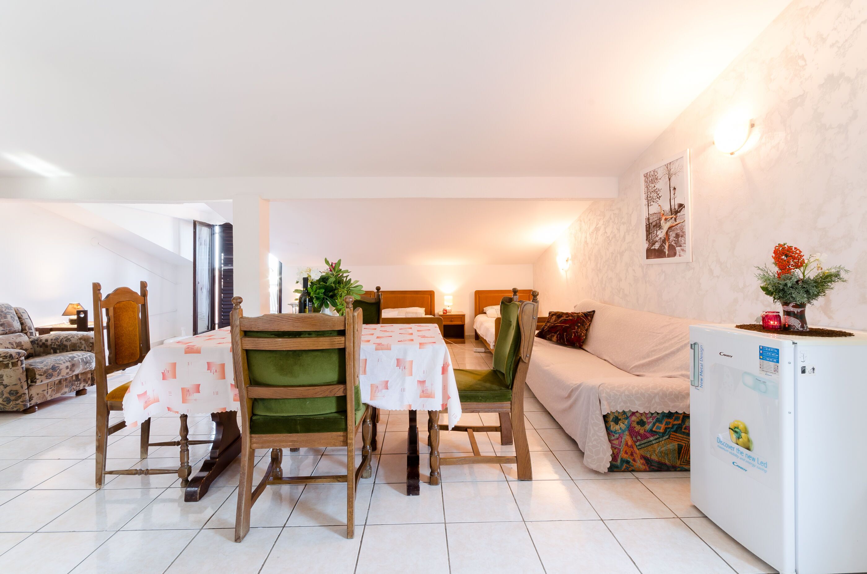 Un salon bien éclairé comprenant un coin repas, un canapé, un lit et un réfrigérateur.
