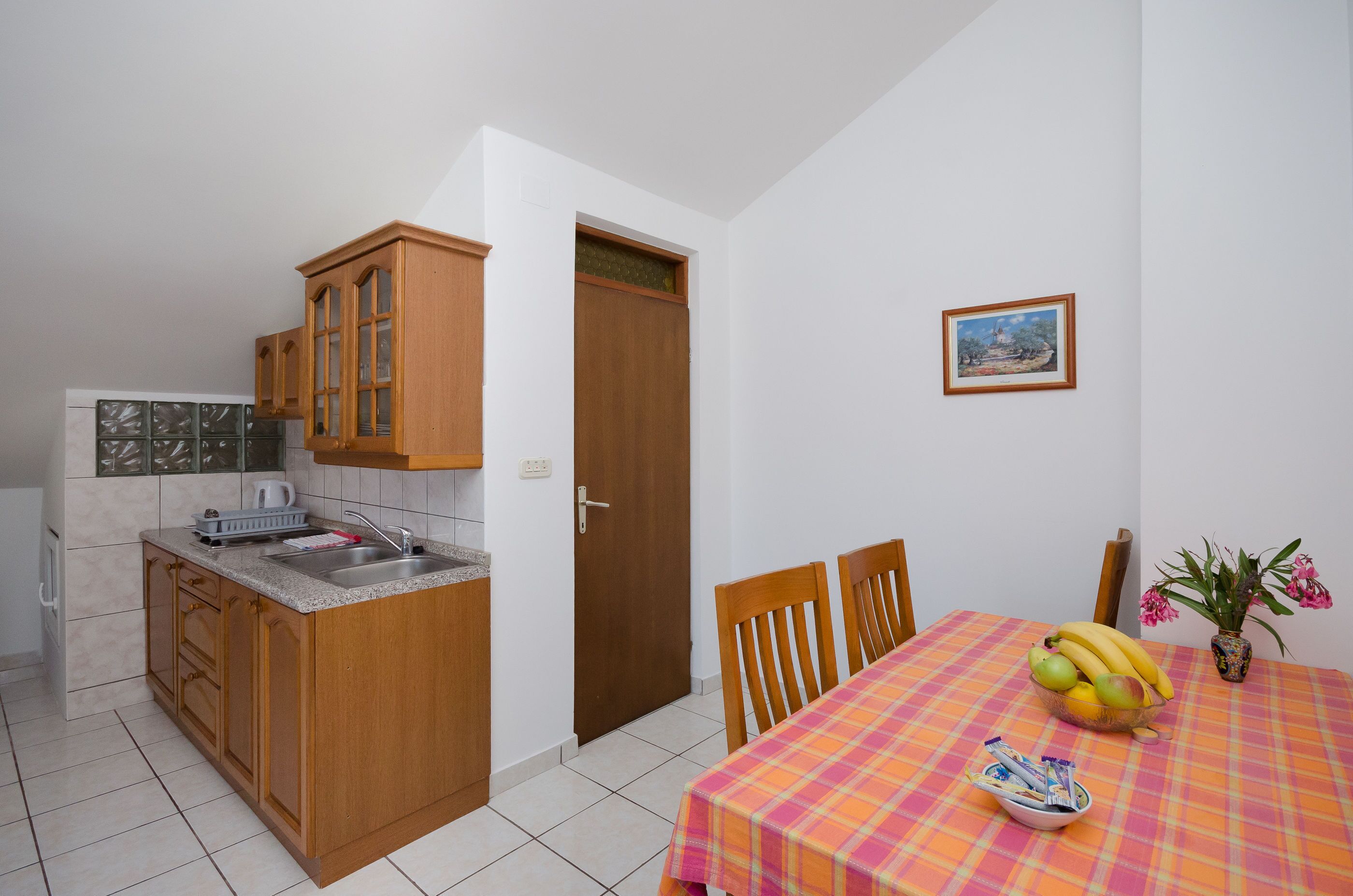 A compact kitchen with wooden cabinets and a tiled backsplash, a dining area with a table set for two, and a small window with a view.