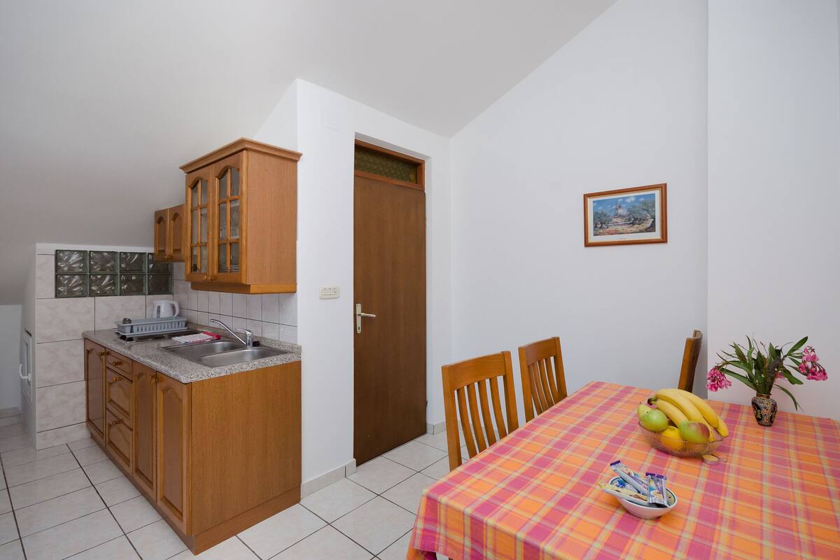 A compact kitchen with wooden cabinets and a tiled backsplash, a dining area with a table set for two, and a small window with a view.