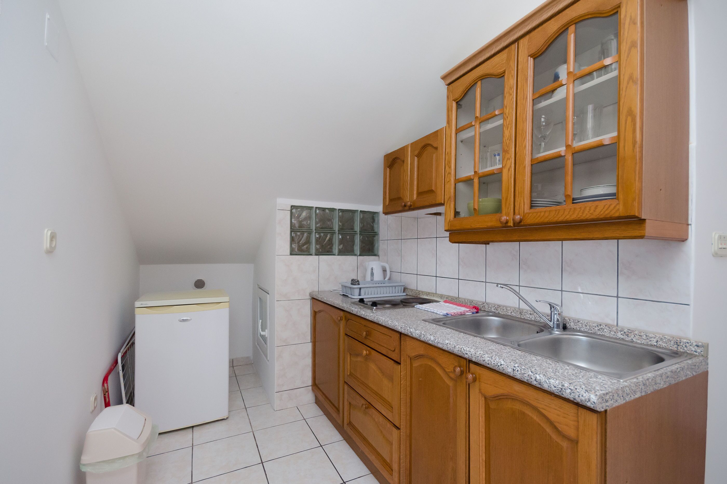 Een kleine keuken met houten kastjes, een dubbele spoelbak en een kleine koelkast.