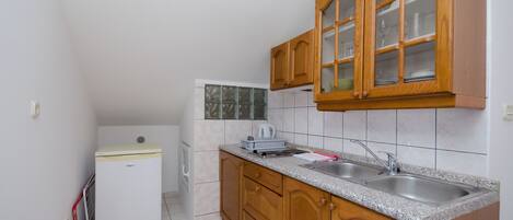 A compact kitchen with wooden cabinets, a double sink, and a small refrigerator.