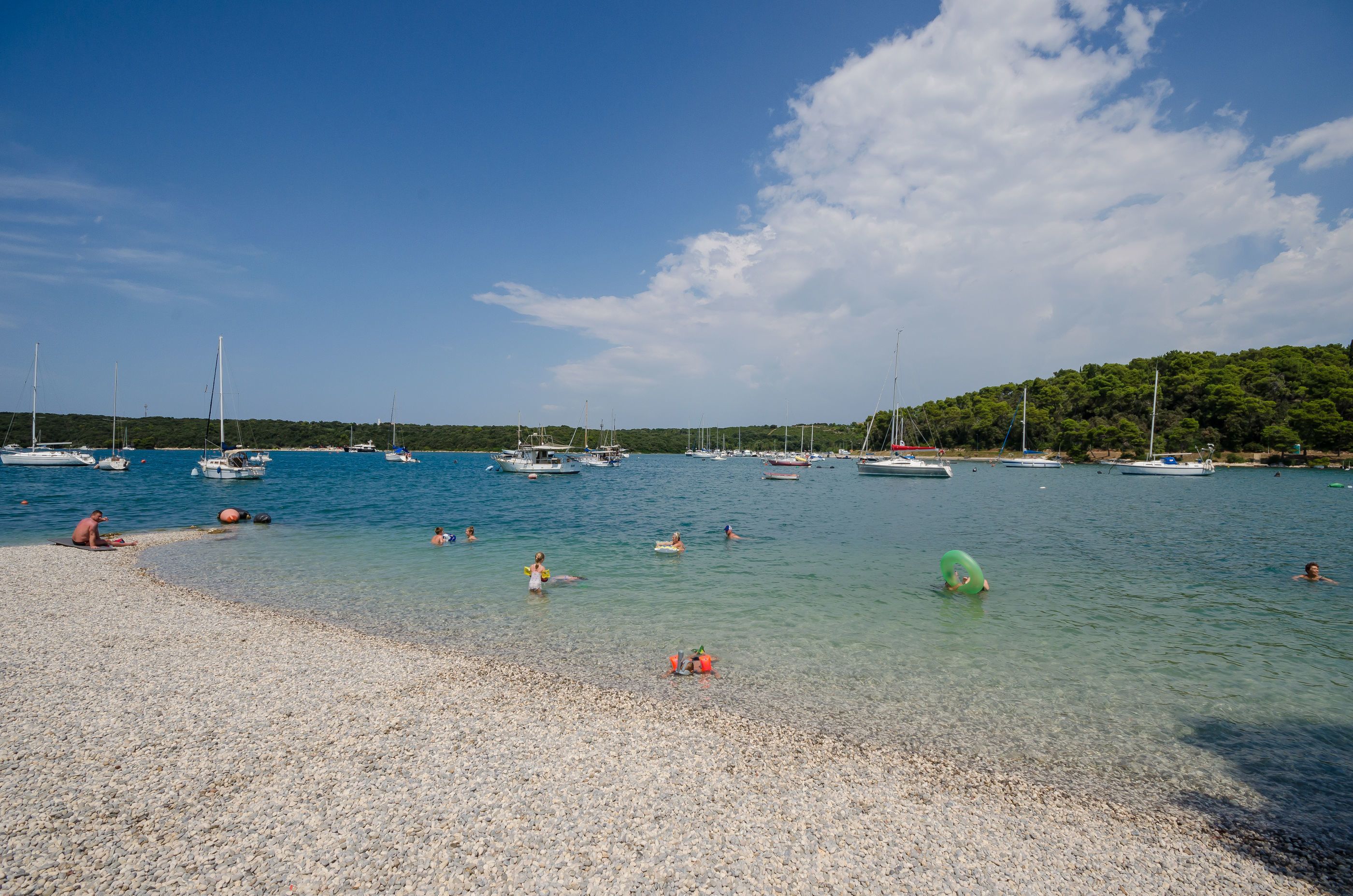 A pebbled beach with boats and people swimming.
