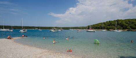 A pebbled beach with boats and people swimming.