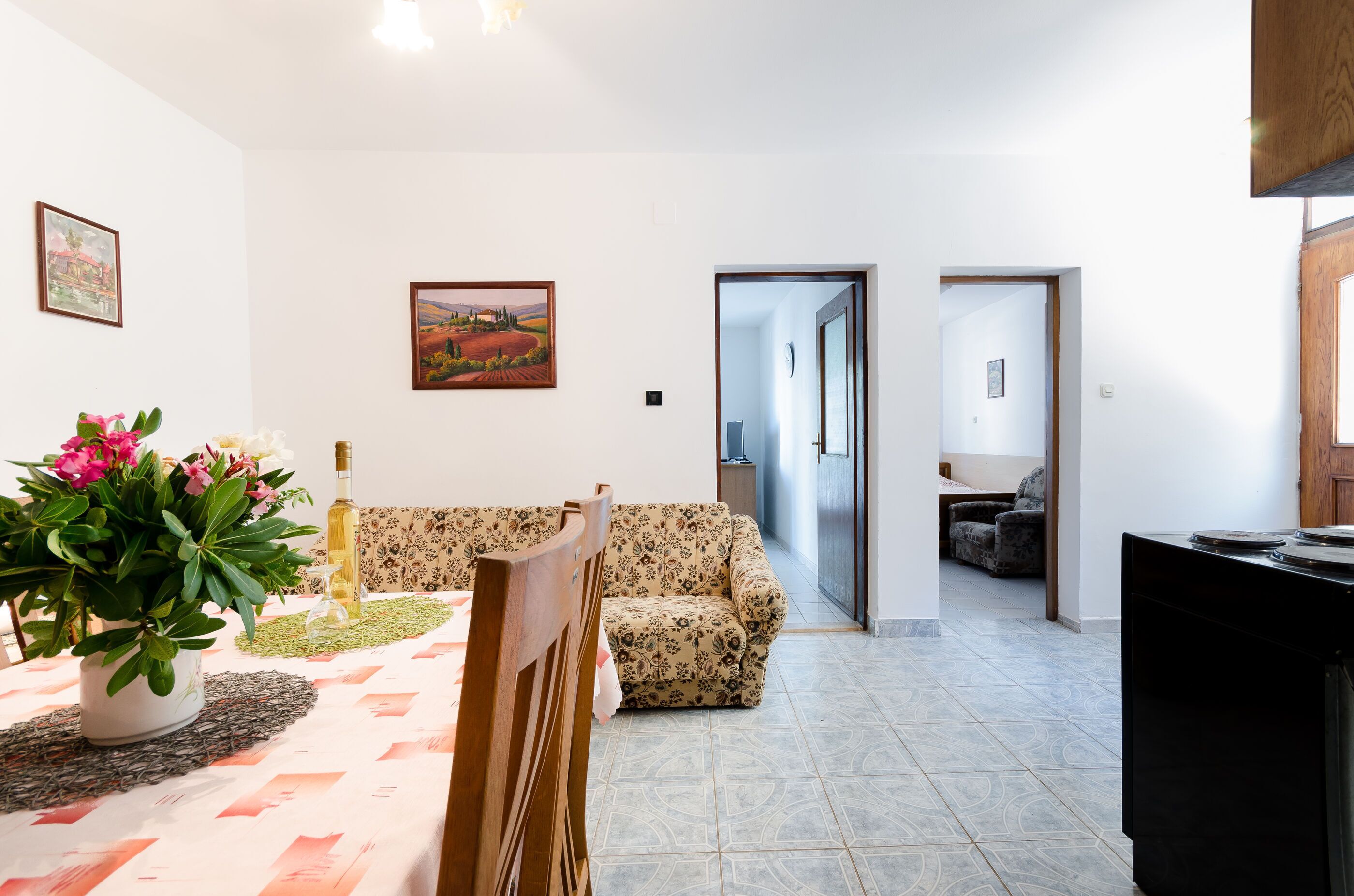 A living room with a sofa, a dining table with a vase of flowers, and a painting on the wall.
