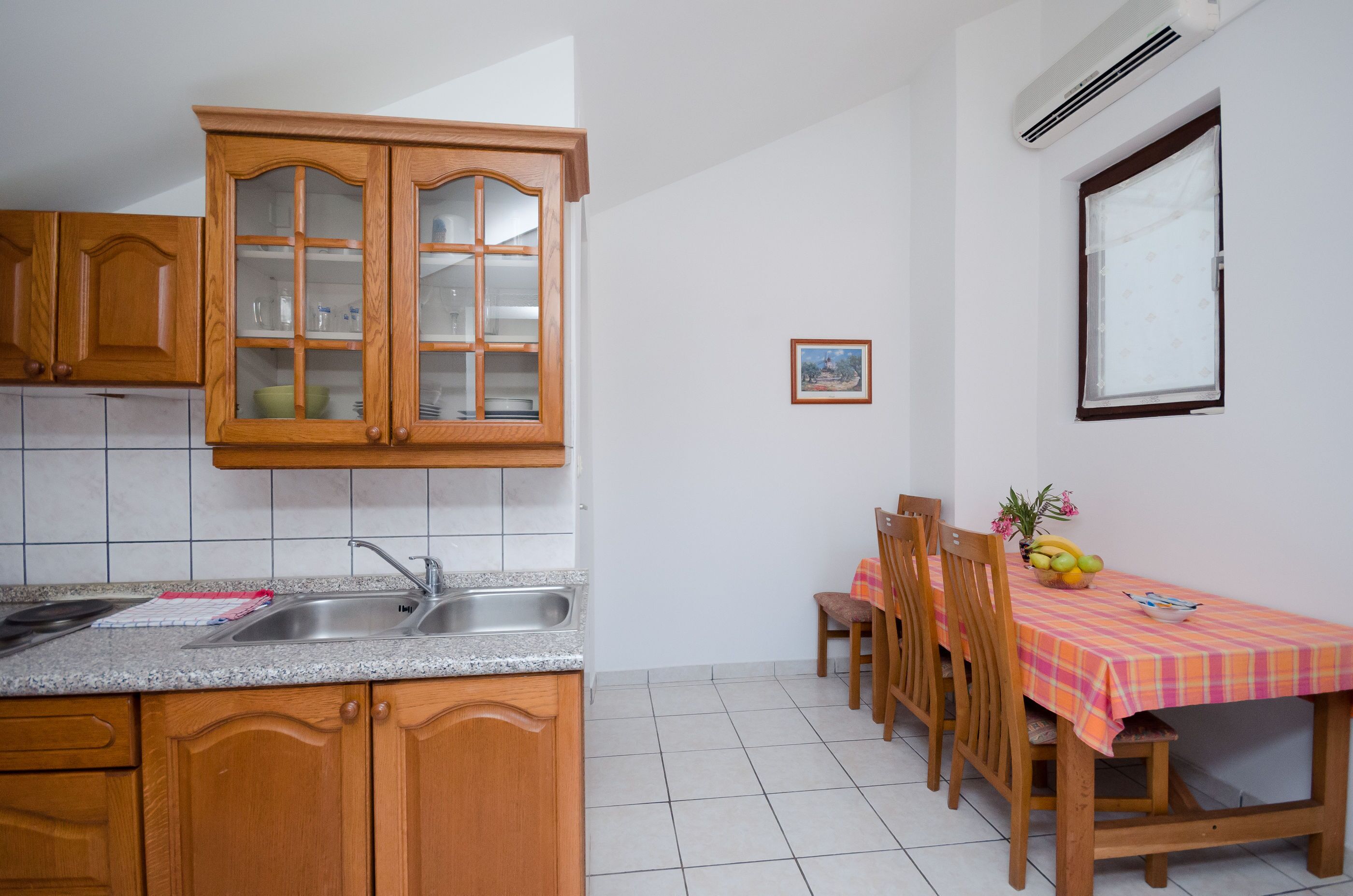 Een keuken met houten kastjes, een granieten aanrechtblad en een eethoek met een tafel en stoelen.