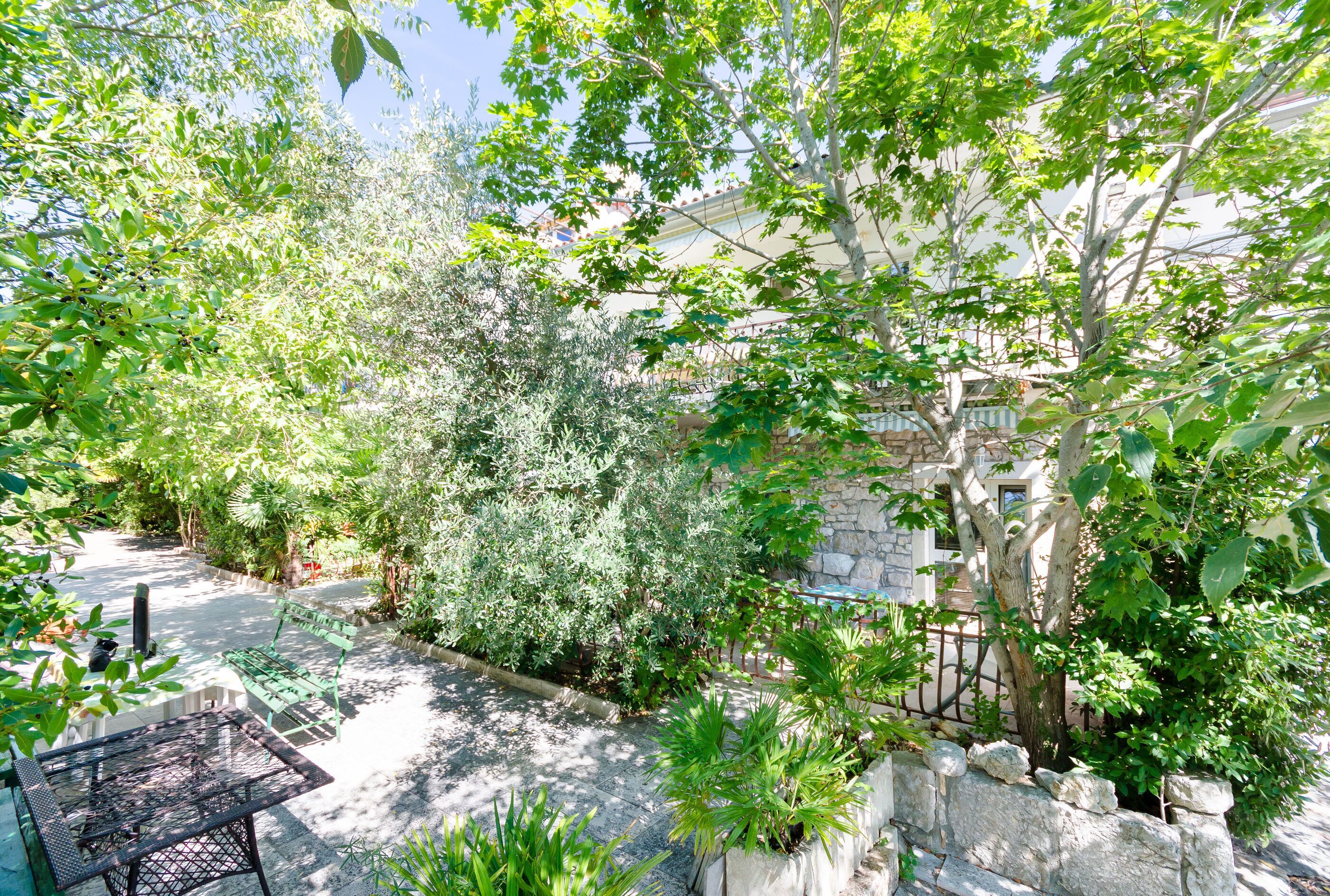 A garden with a stone wall, a metal table, and various plants.