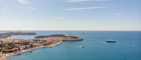 An aerial view of a coastal town with a prominent lighthouse, marina, and clear blue sea.