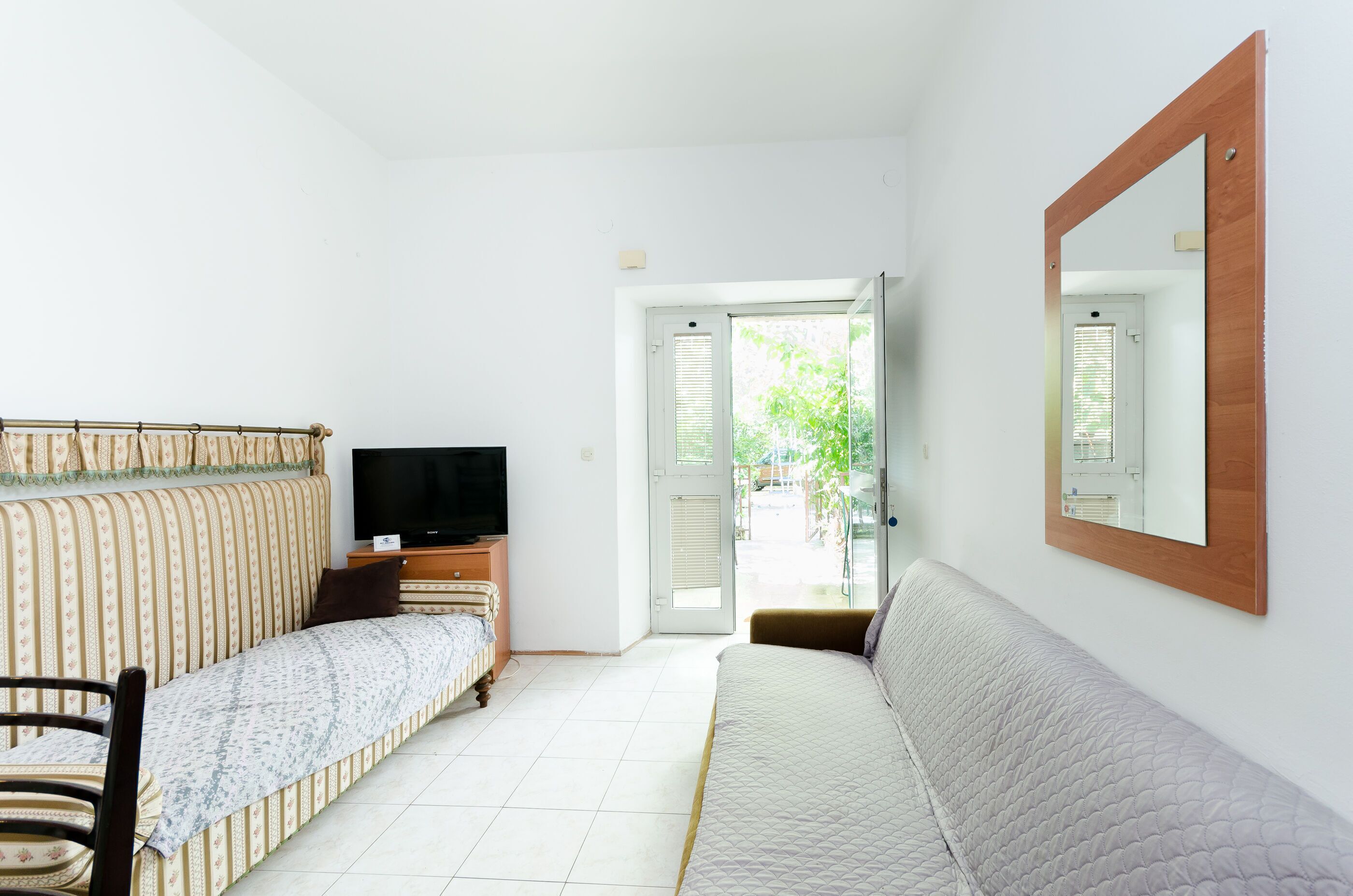 A room with a bed, a sofa, a TV, and a door leading outside.