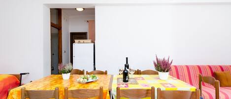 Un coin repas avec une table dressée pour deux personnes, des chaises, une plante en pot et une bouteille de vin.