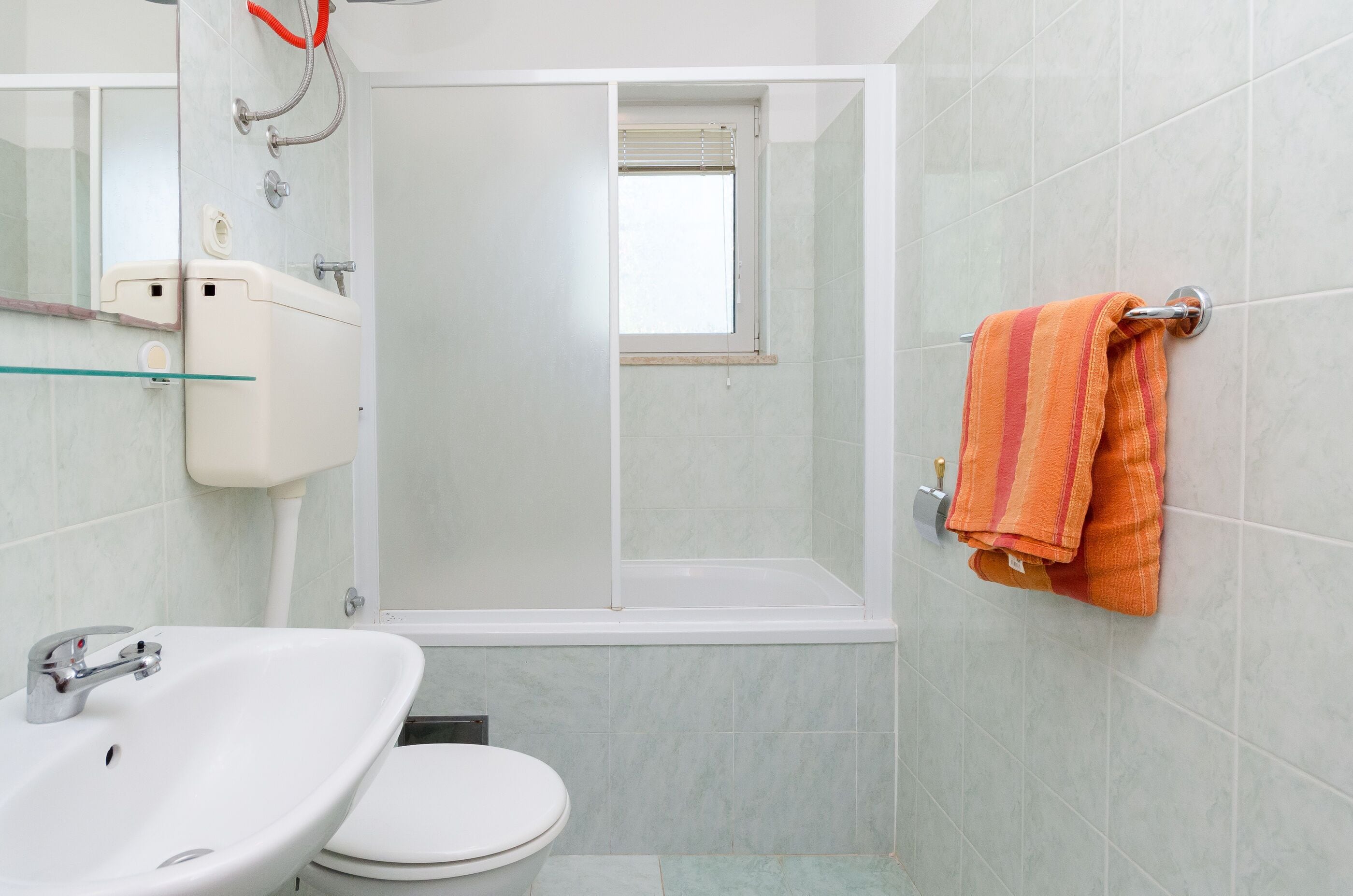 A bathroom with a white sink, toilet, and a shower with a window.