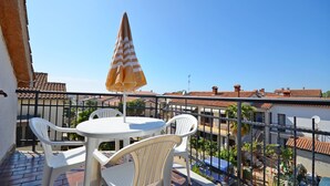 Een balkon met een tafel en stoelen, een geribbelde parasol en uitzicht op omliggende gebouwen.