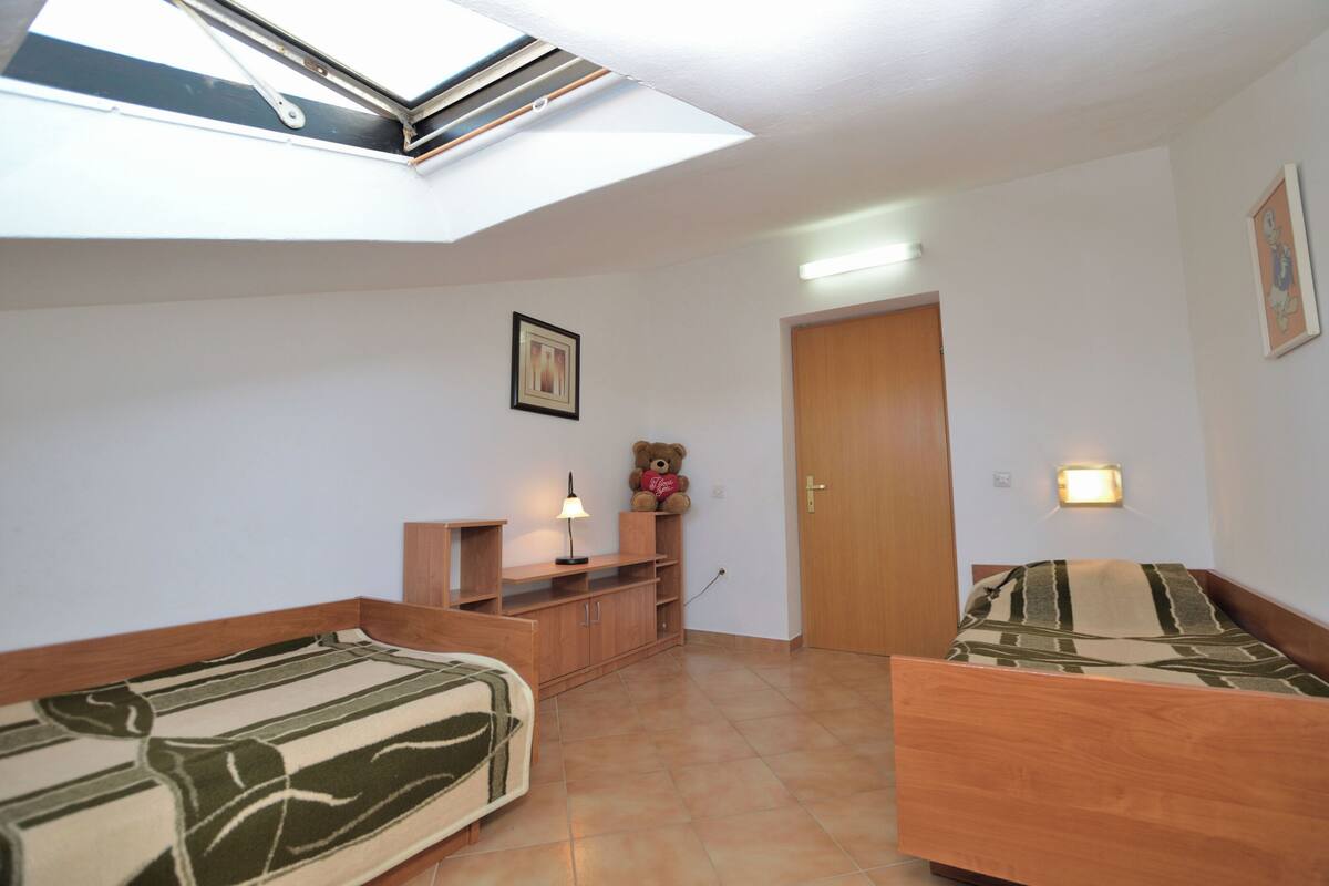 A small, well-lit room with a skylight, a bed, a sofa, a teddy bear, and a lamp.