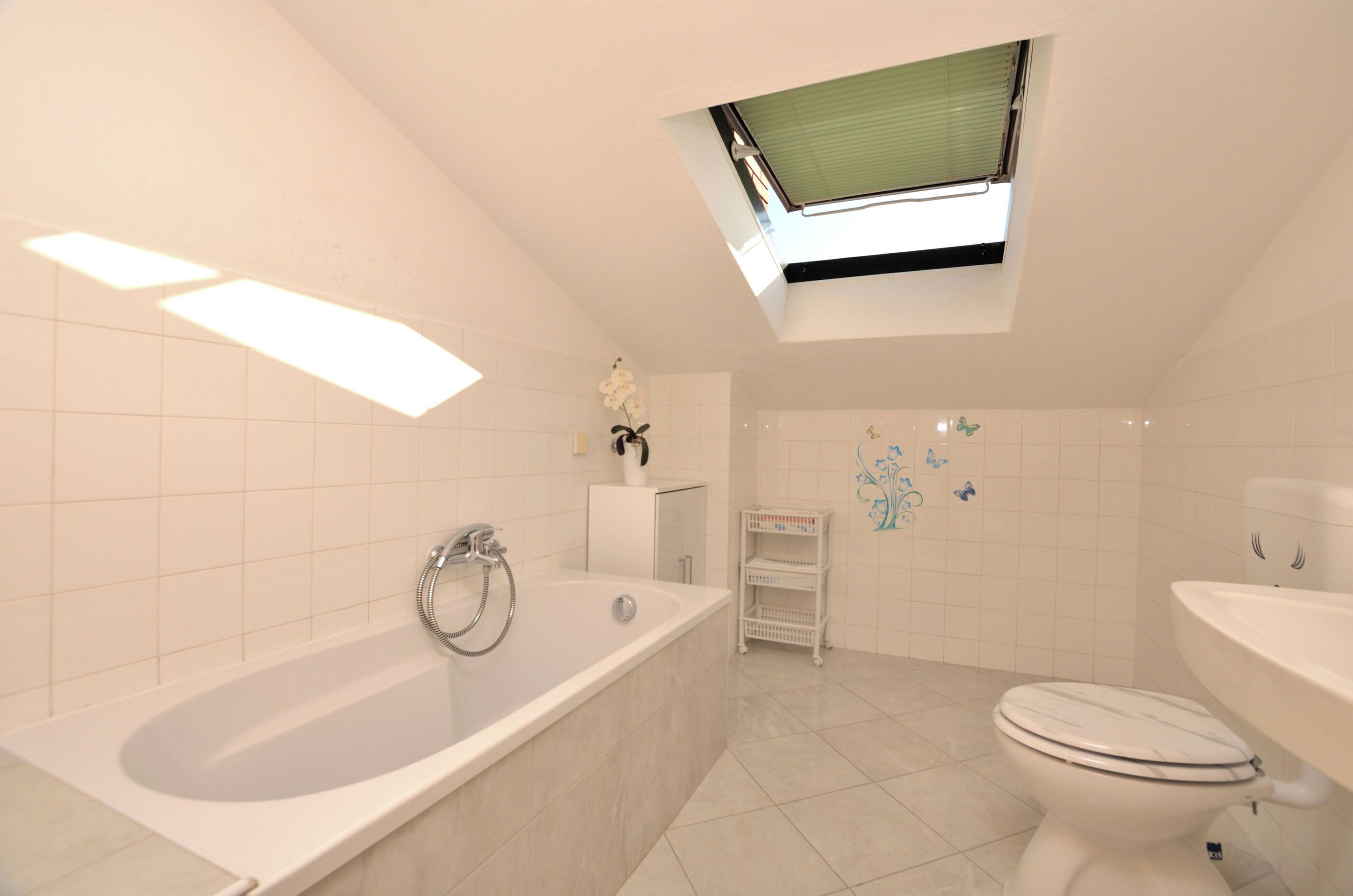 Un baño moderno con tragaluz, una bañera, un inodoro y un pequeño estante con artículos de aseo.