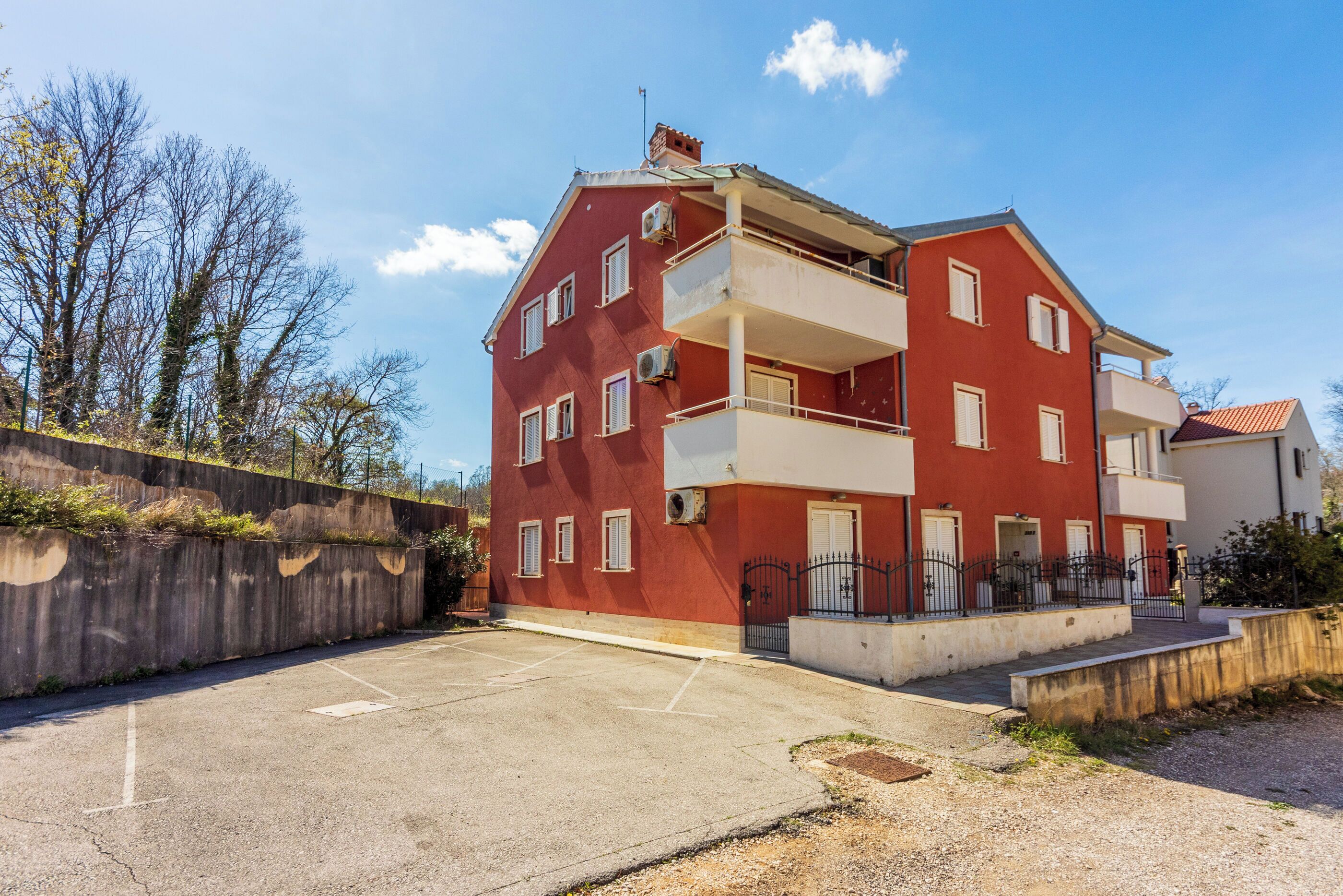 Un immeuble rouge à plusieurs étages, doté de balcons, d’un espace de stationnement et d’un mur en béton recouvert de végétation.