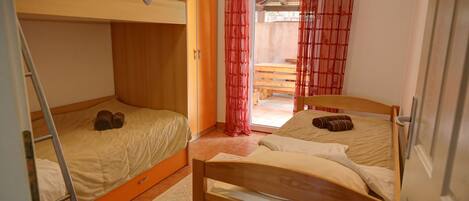 A dormitory room with two bunk beds, a wooden wardrobe, a ladder, and a window with red curtains.
