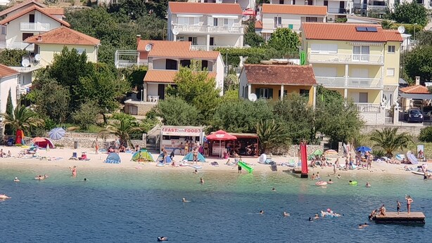 A coastal town with a beach, buildings with red roofs, and a 'PASTO' sign. - Apartments Ivat (Rogoznica)