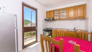 A compact kitchen with wooden cabinets, a gas stove, and a dining table with a red tablecloth. - Apartments Ivat (Rogoznica)