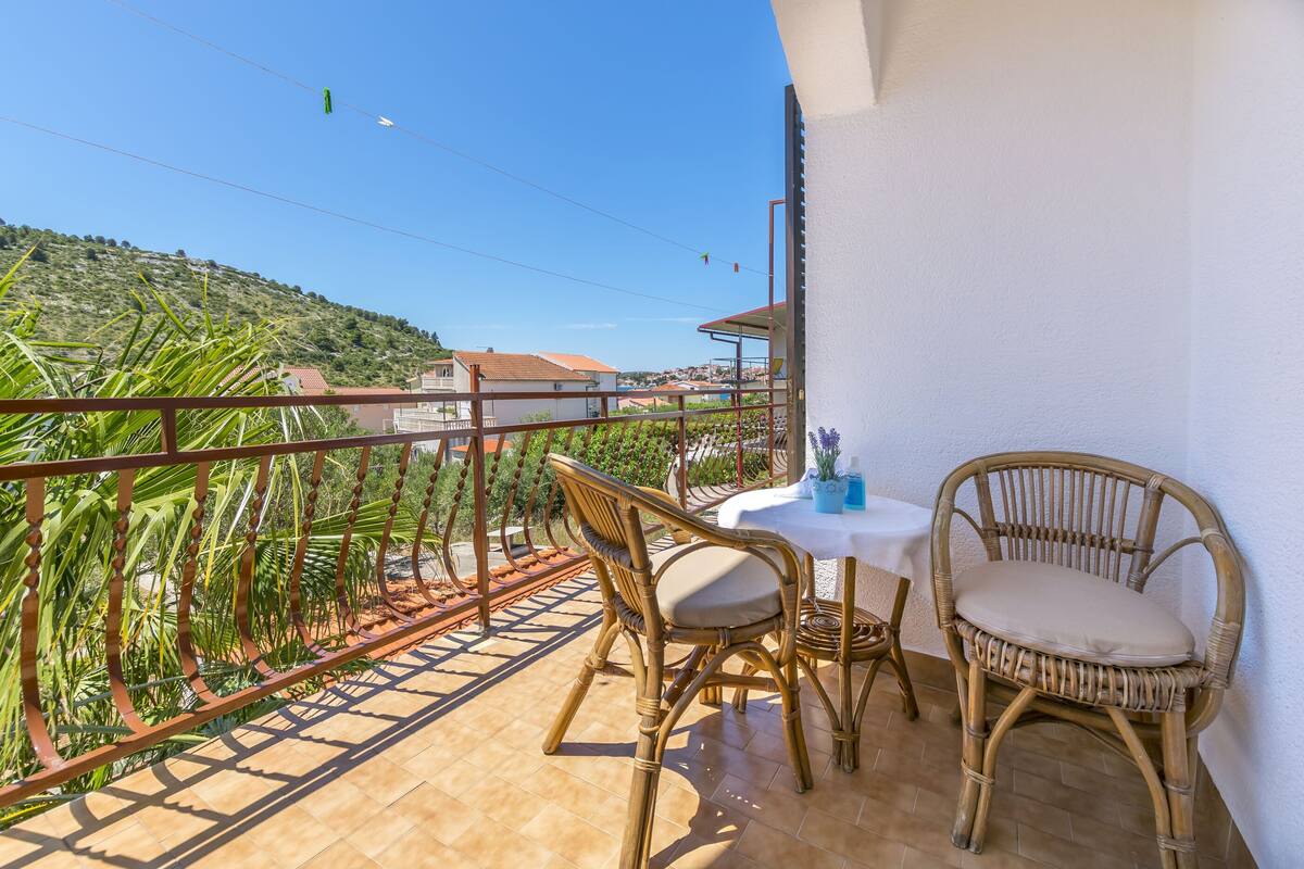 A balcony with wicker furniture, a table, and a view of a hillside.