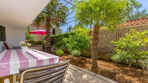 A patio with a table and chairs, surrounded by greenery and a stone wall. - Apartments Ivat (Rogoznica)