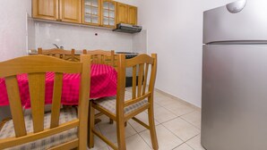 A compact kitchen with wooden cabinets, a stainless steel refrigerator, and a dining table with chairs. - Apartments Ivat (Rogoznica)