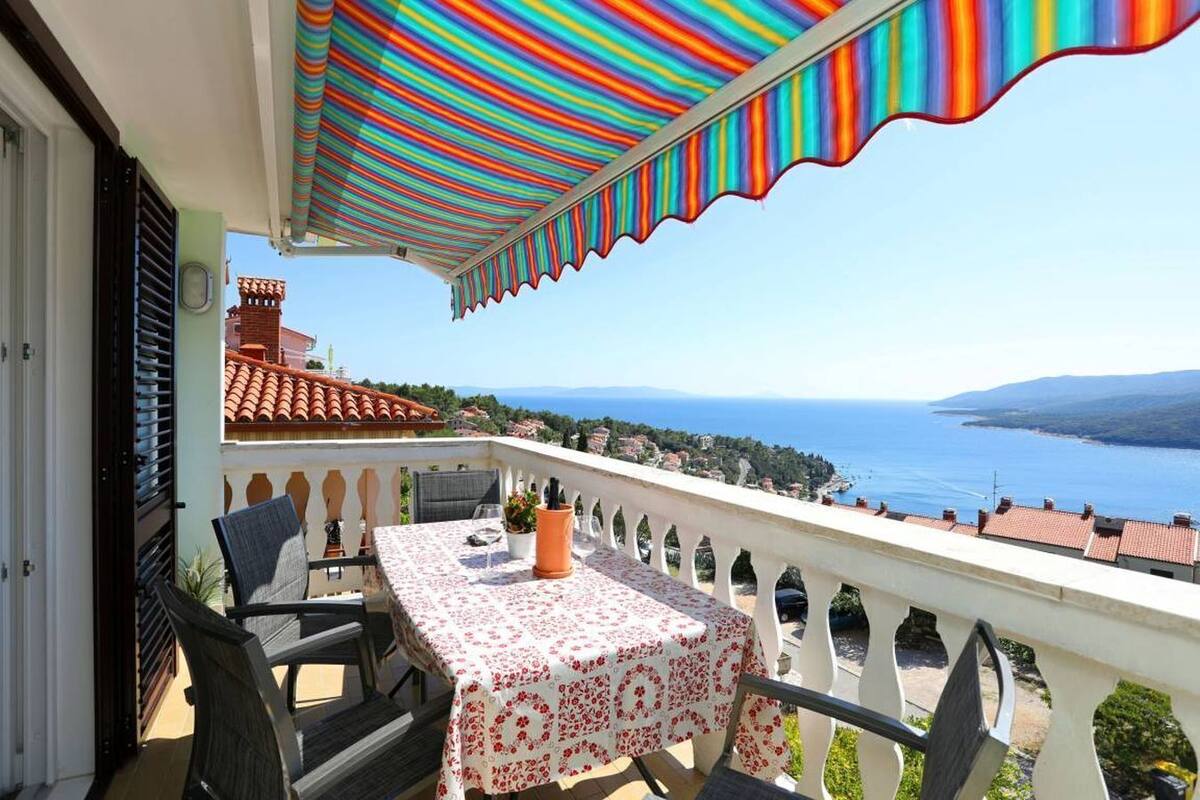A balcony with a table and chairs, a view of the sea, and a colorful striped awning.