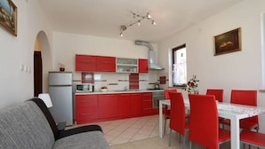 Une cuisine de taille réduite avec des meubles rouges, une table à manger avec des chaises rouges, un canapé gris et un luminaire blanc au plafond.