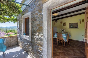 A stone building with a balcony, a dining area with a table and chairs, and a view of the landscape. - House Dorino (Krsan)