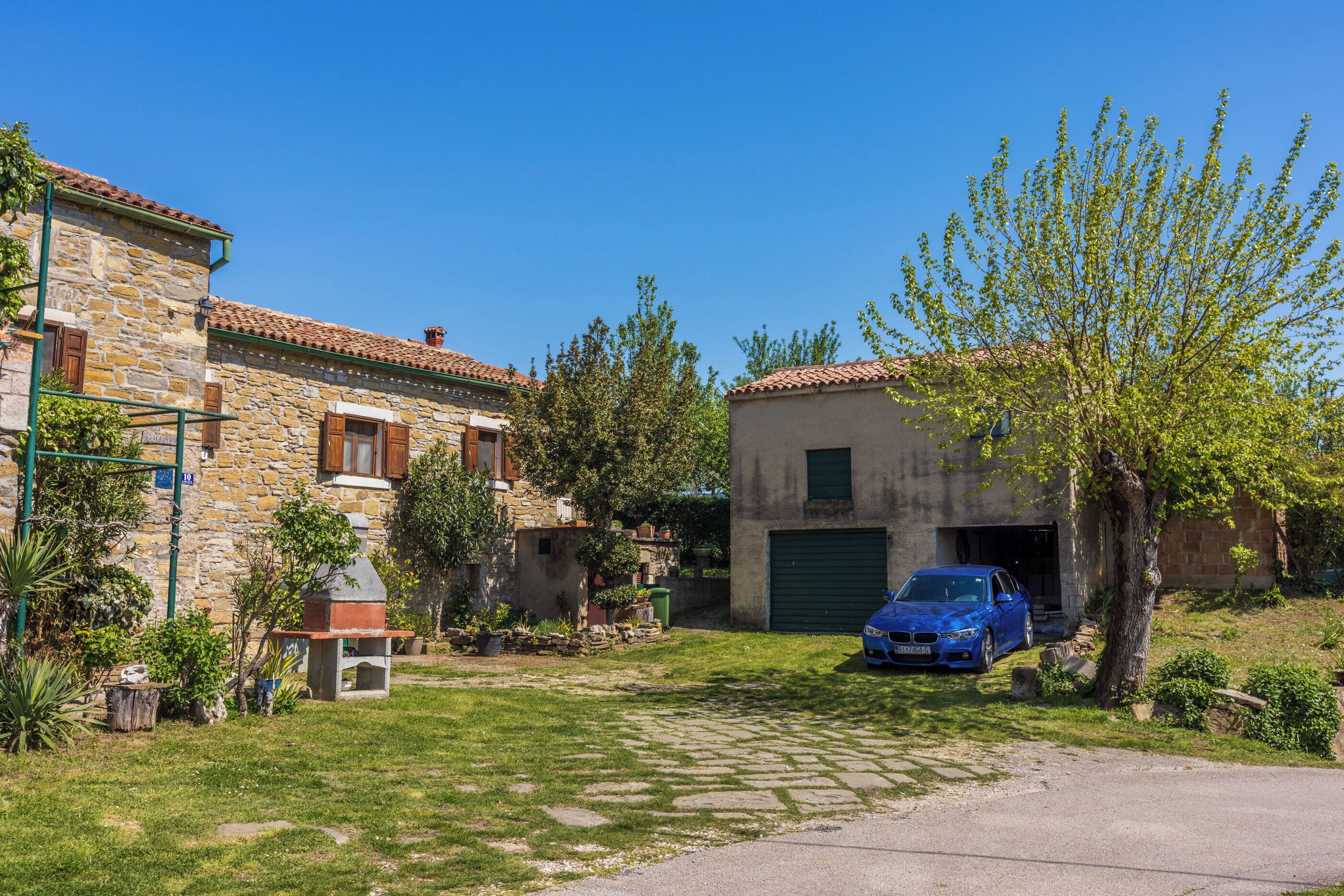 A stone house with a garage, a barbecue, and a blue car parked in the driveway.