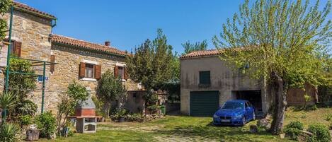 A stone house with a garage, a barbecue, and a blue car parked in the driveway.