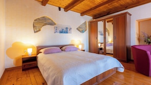 A bedroom with a wooden floor, a bed with a white bedspread, two bedside lamps, and a wooden wardrobe. - House Dorino (Lanisce Krsan)