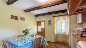 A cozy kitchen with a dining table set for two, wooden chairs, a stove, and a window with curtains. - House Dorino (Lanisce Krsan)