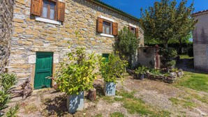 A stone building with wooden shutters, a green door, and potted plants in the courtyard. - House Dorino (Lanisce Krsan)