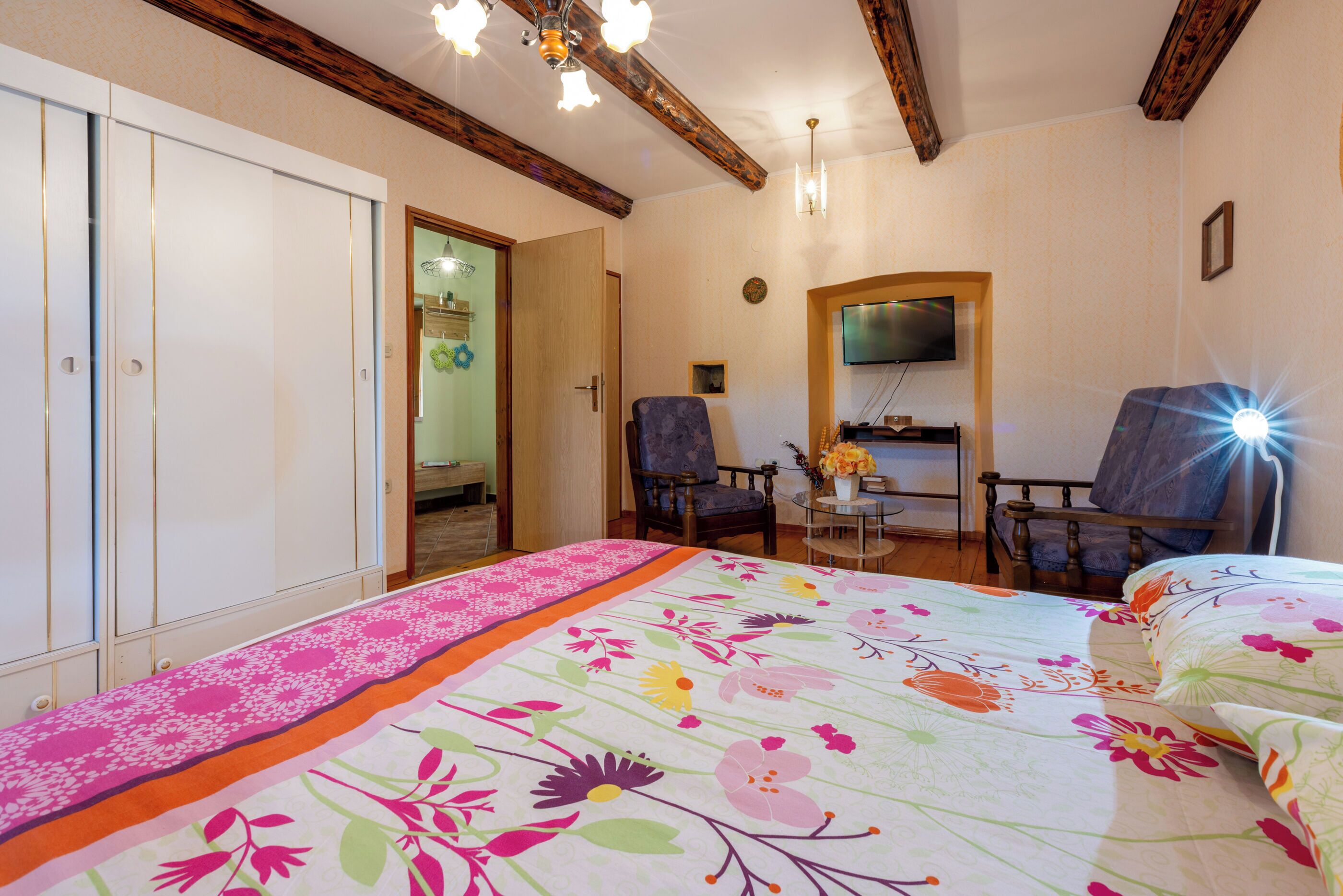 Een slaapkamer met een bed, twee stoelen, een televisie en een houten plafond.