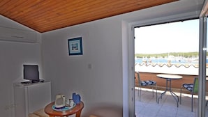 A room with a wooden ceiling, a television on a cabinet, a small table with a kettle, and a view of a marina with boats. - Apartments and Rooms Viktorija (Pjescana uvala)