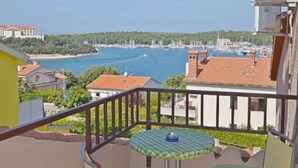 A balcony with two chairs and a small table, overlooking a marina with boats and a clear blue sky. - Apartments and Rooms Viktorija (Pjescana uvala)