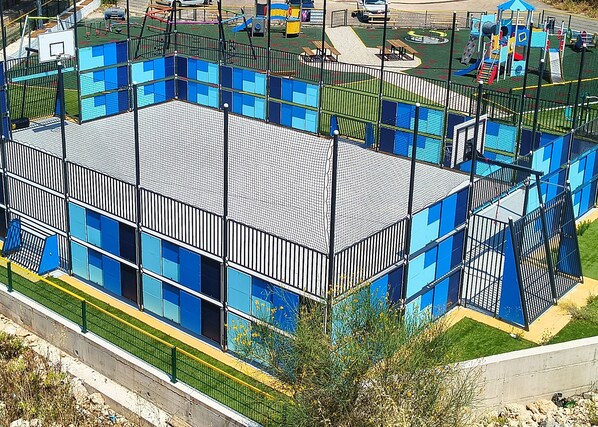 A multi-story building with a modern design, featuring a mix of glass and metal elements, and surrounded by a green fence.