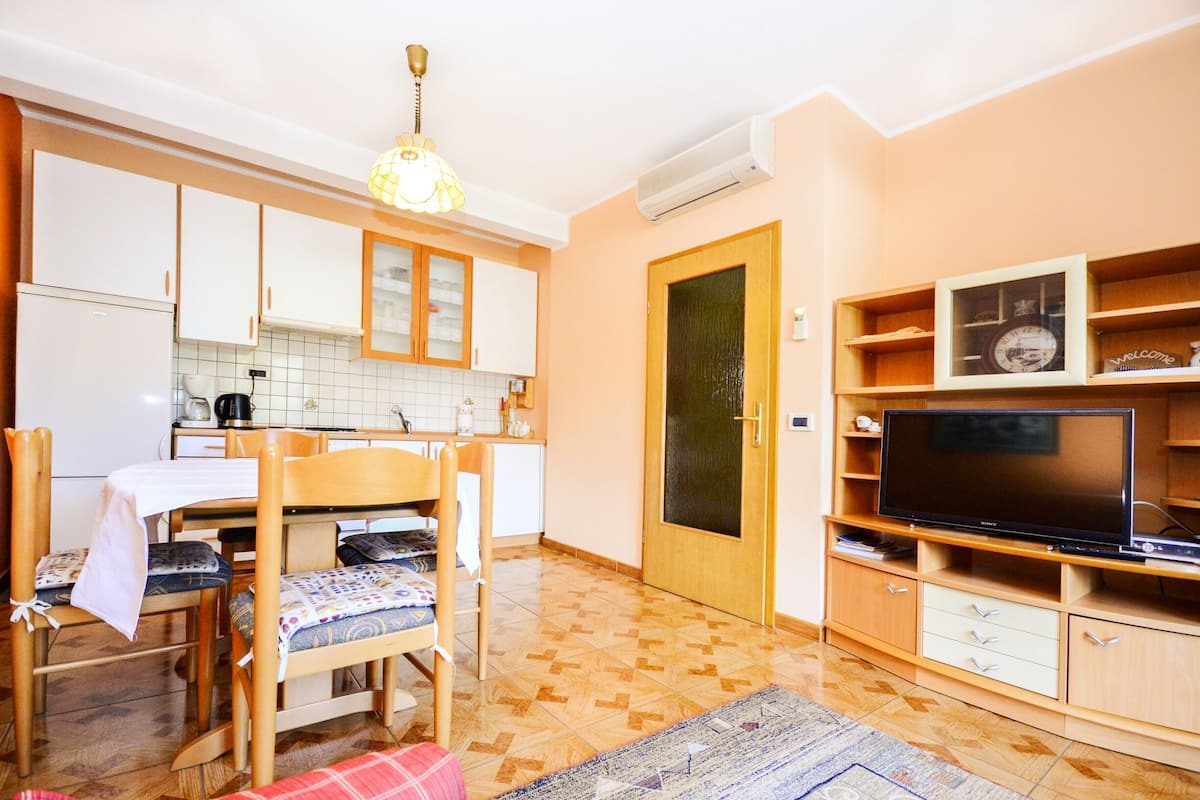 A compact kitchen with a dining area, a TV on a wooden stand, and a door with a glass panel.