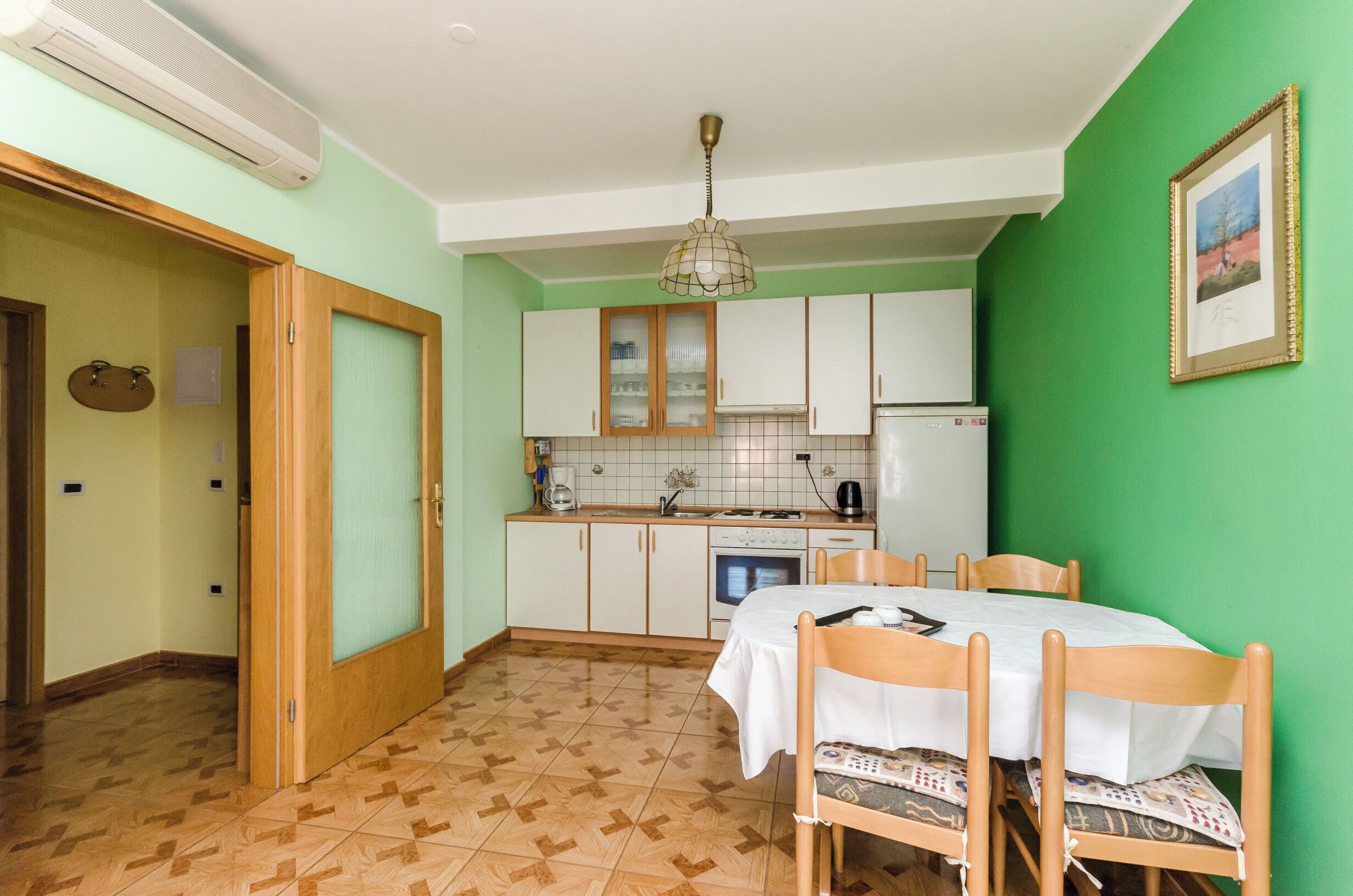 A compact kitchen with white cabinets, a dining table with chairs, and a green wall.