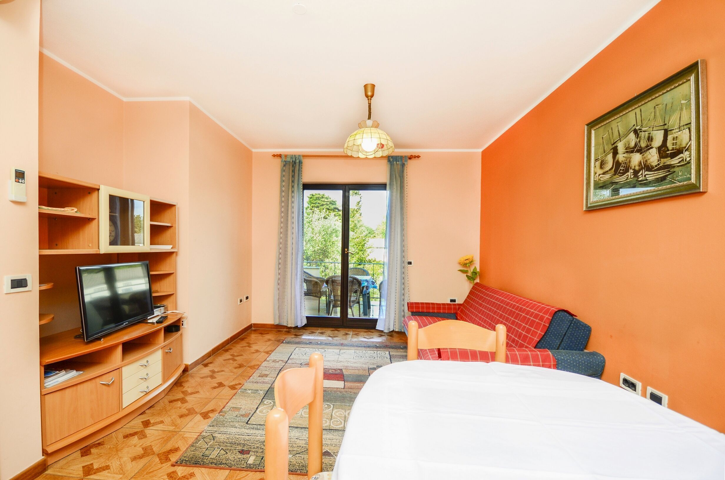 Ein Schlafzimmer mit Bett, Fernseher, Schreibtisch und einem fensterbepflanzten Fenster.