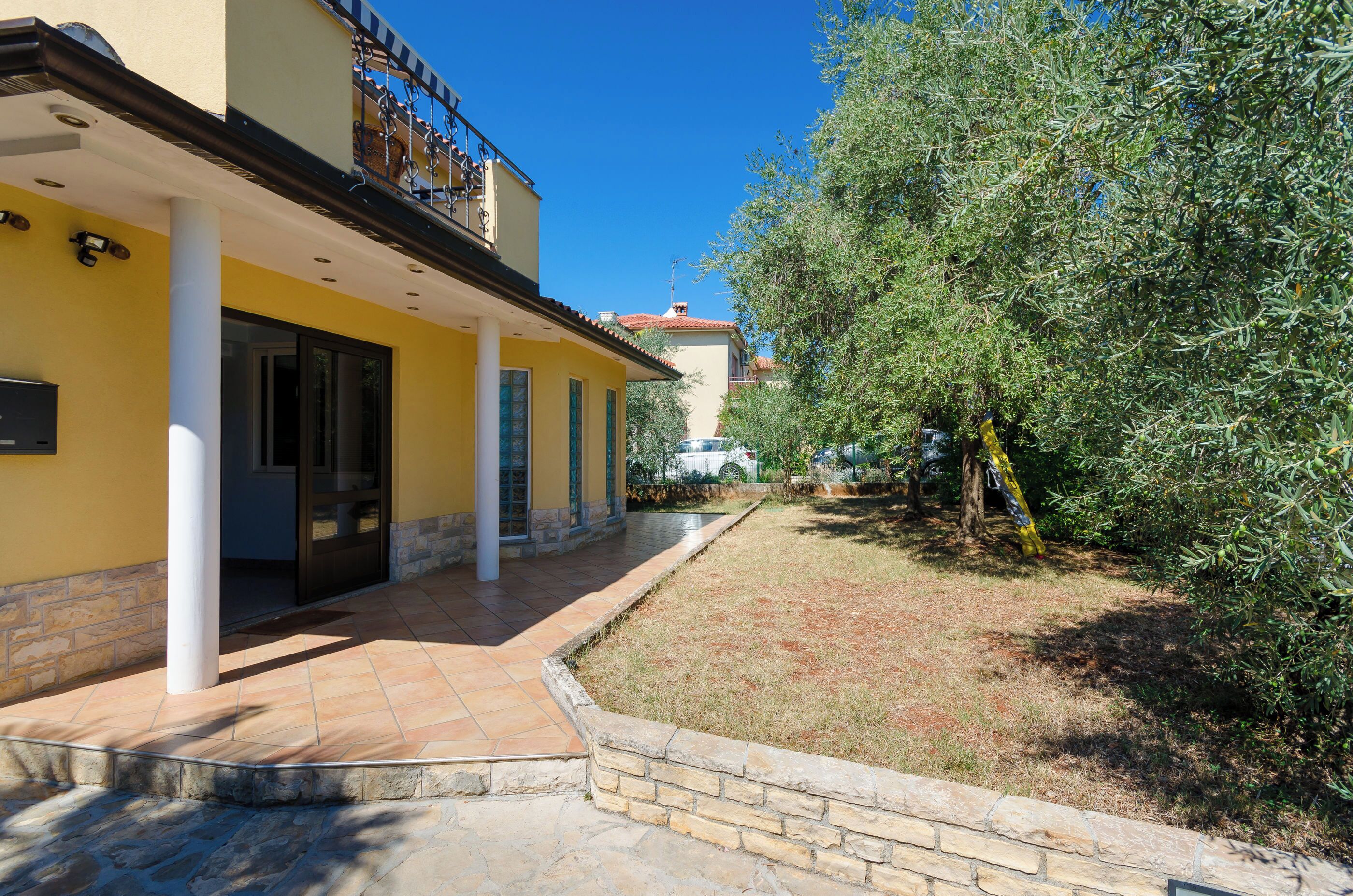 A yellow building with a covered patio area, stone columns, and a stone pathway leading to the entrance.