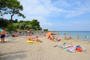 A beach with people sunbathing, swimming, and playing. - Apartments Marija (Umag)