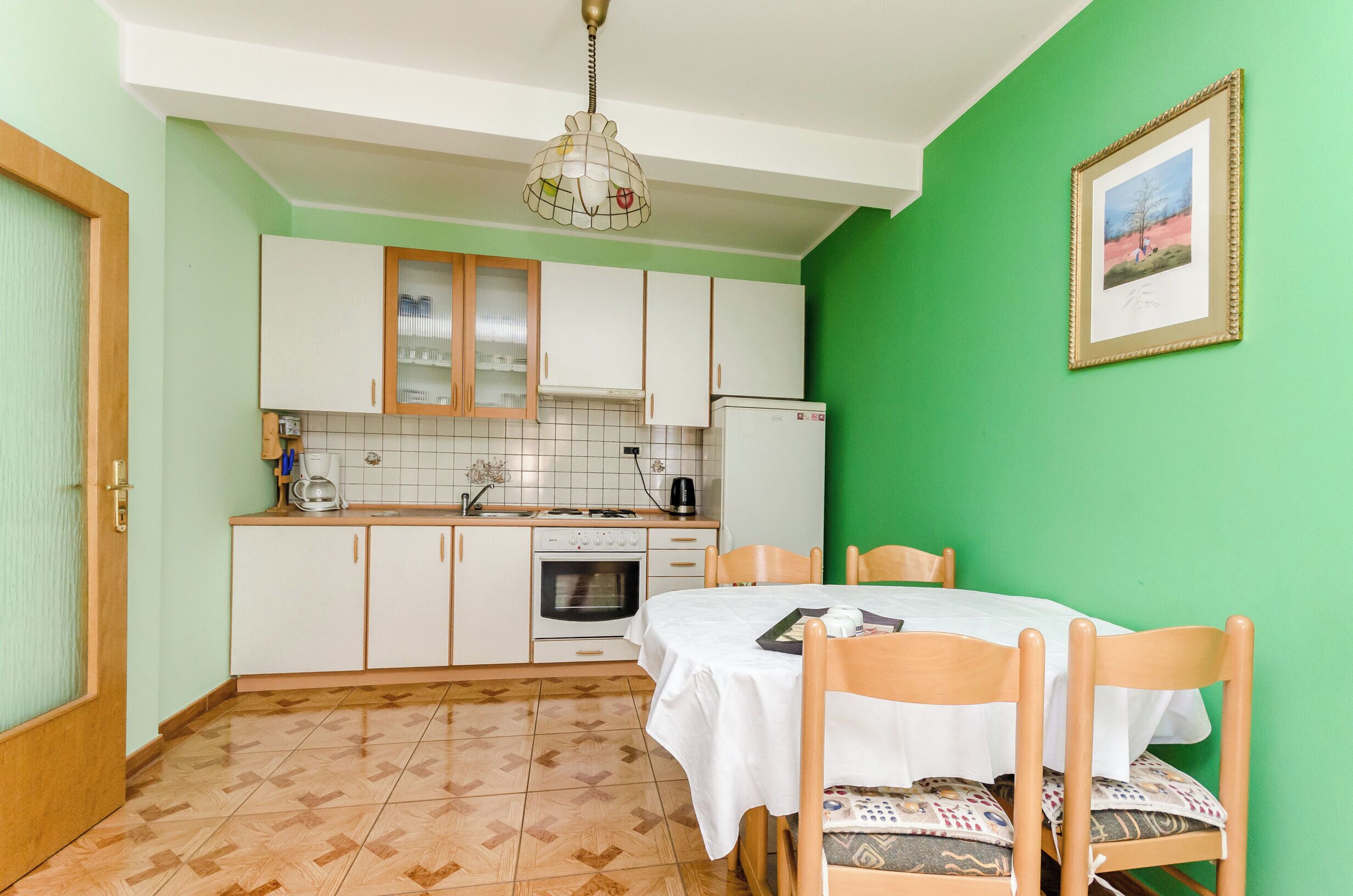 A compact kitchen with white cabinets, a tiled backsplash, a sink, a stove, and a dining table with chairs.