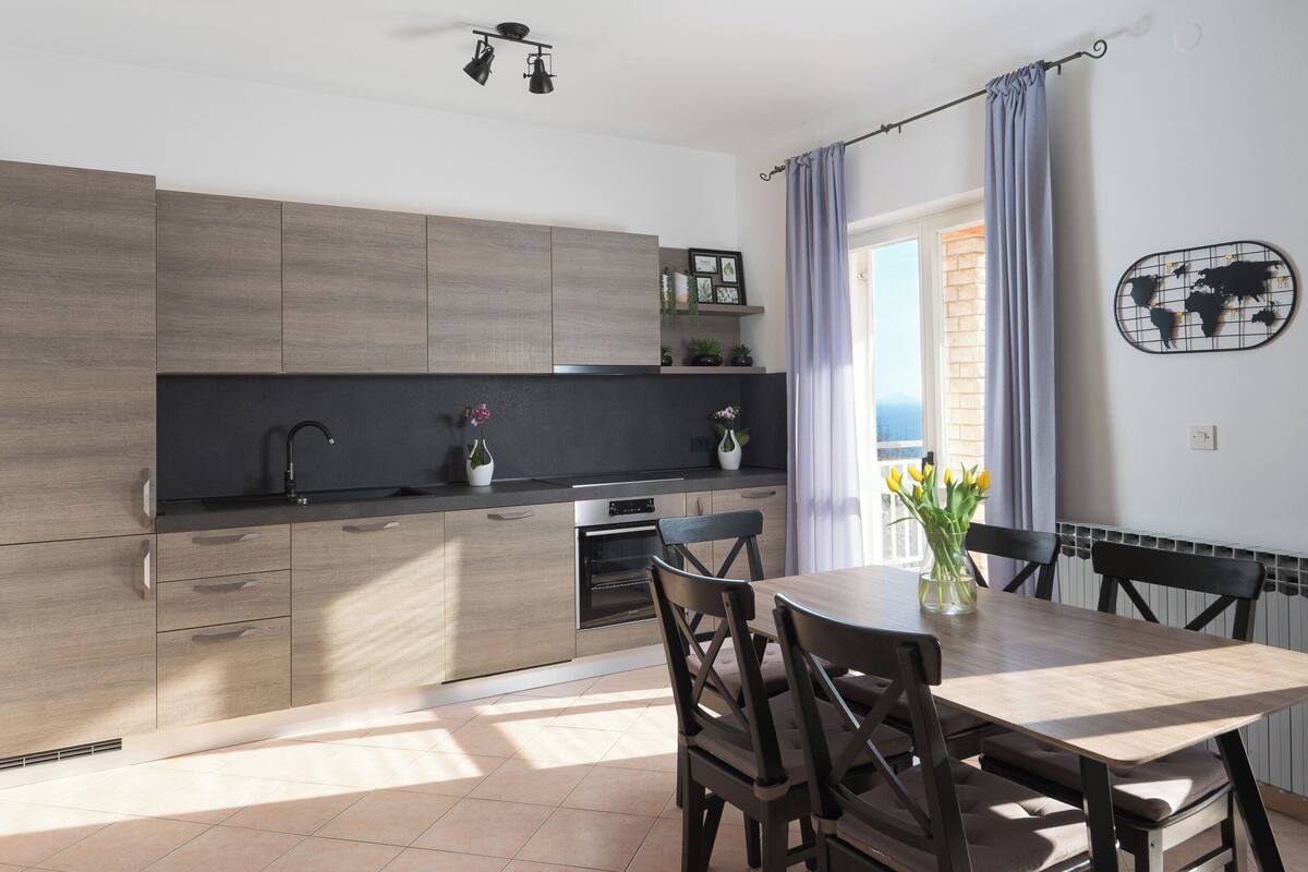 A modern kitchen with wooden cabinets, a black countertop, and a dining area with a wooden table and chairs.