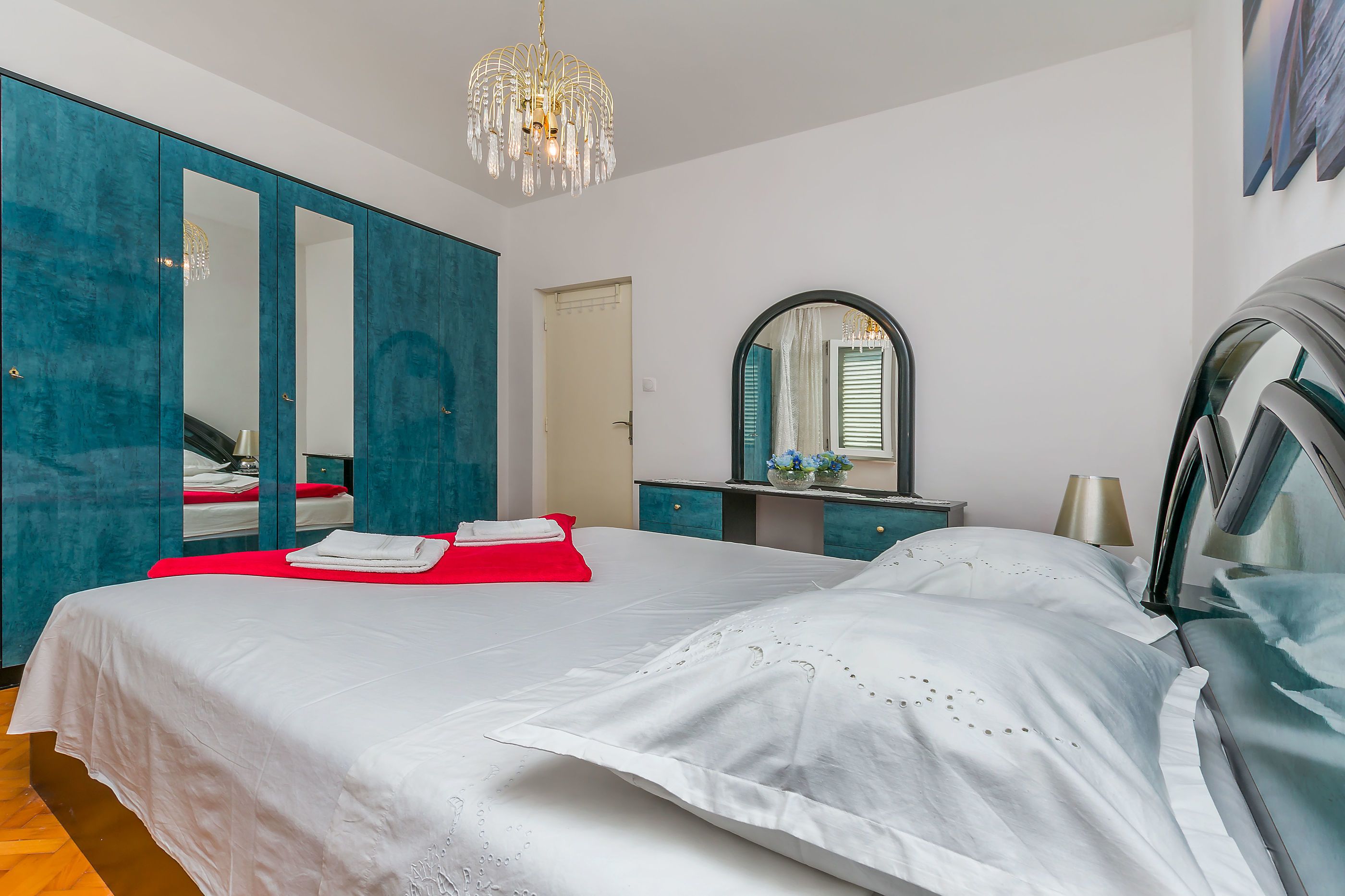 Ein Hotelzimmer mit einem großen Bett, einem Kleiderschrank, einem Schminktisch mit Spiegel und einer Kristallleuchter.