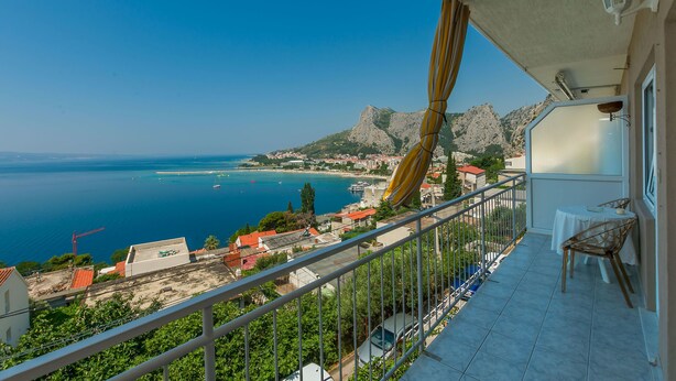 A balcony with a view of the sea, a mountain, and a town.