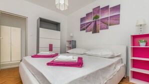 A bedroom with a bed, white and pink shelving, a wardrobe, and artwork on the wall.